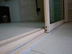 Homeowner struggling to open a sliding door with worn rollers and a dirty track.